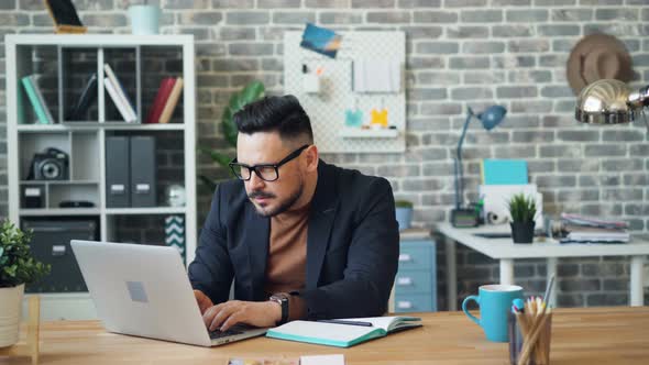 Young Man Using Internet To Find Information Then Writing in Notebook