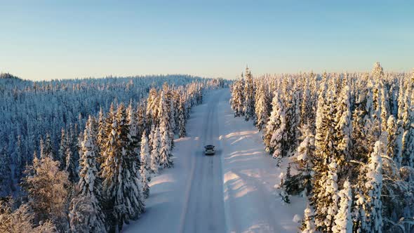 Aerial view following vehicle driving long snowy frozen road trail between Norbotten Lapland winter