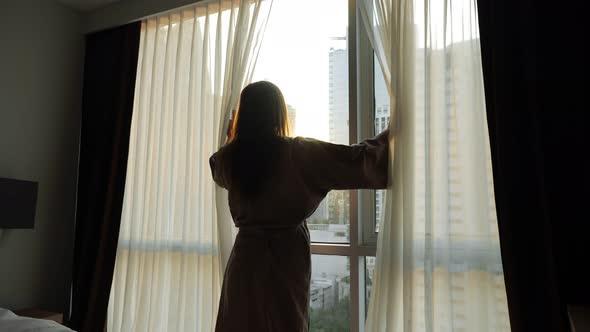 Young Girl in Bathrobe Opens Window Transparent Curtains in Apartment