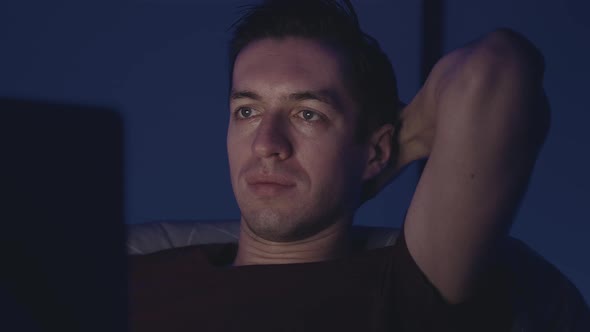 Young Man Watching a Movie on a Laptop on a Bed at Night