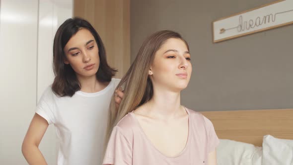 Attractive Girl Making a Ponytail for Her Friend While Having a Rest in Bedroom