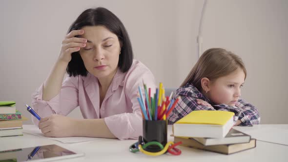 Side View of Brunette Caucasian Woman Sitting Back To Back with Daughter and Signing. Upset Mother