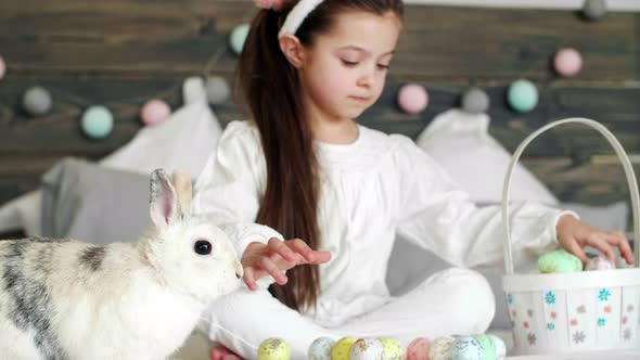 Girl playing with rabbit and easter eggs on the bed