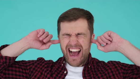 Angry Man Shouting and Covering His Ears with His Hands Isolated on a Turquoise in the Studio