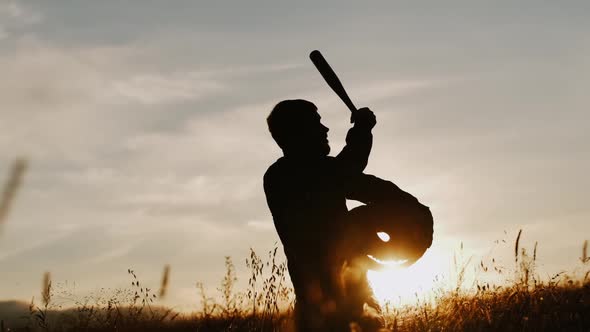 Silhouette of a Man Against the Backdrop of a Sunset Holding a Large Halloween Pumpkin and a Bat in