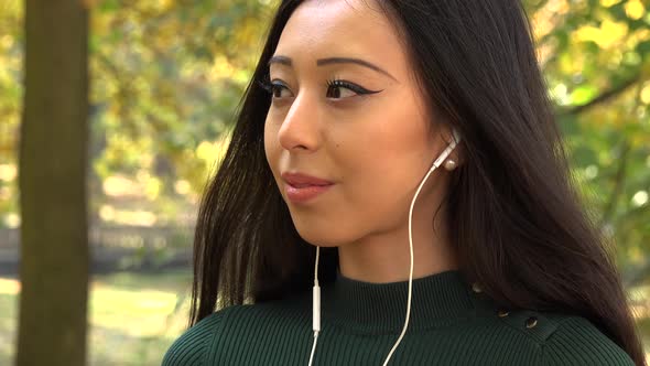 A Young Asian Woman Listens to Music on A Smartphone in A Park