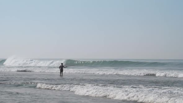 Local Fisherman Holds Rod in Hand in Waving Blue Ocean