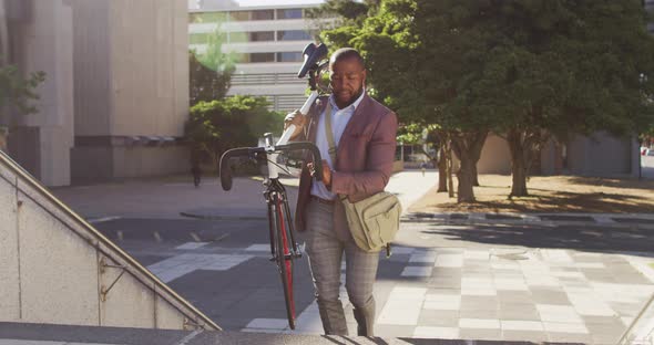 Happy african american man carrying bike upstairs in city