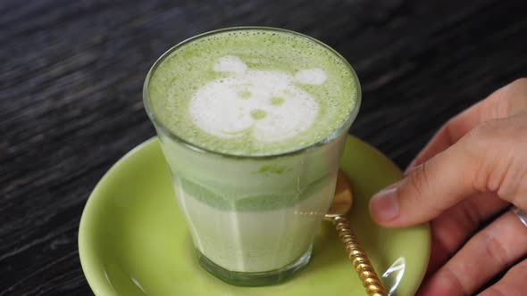 Hand Taking Away a Glass of Matcha Tea Latte with Bear Face Foam Art on It