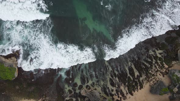 Top down aerial view of giant ocean waves crashing and foaming in coral beach