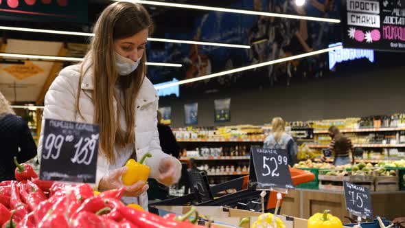 Woman in a protective mask in the supermarket buys oranges.