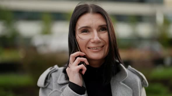 Portrait of a Brunette in a Gray Coat Against a Background of Blurred Modern Buildings