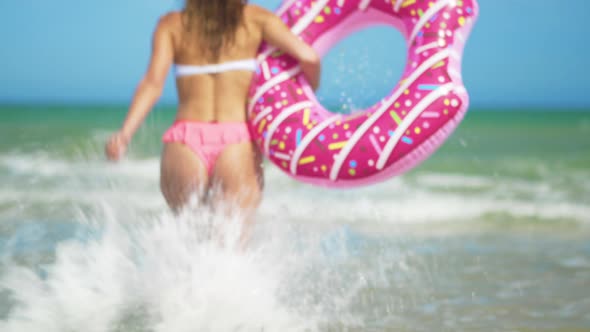 Young Woman Having Fun with Toy Inflatable Ring Donut on the Beach