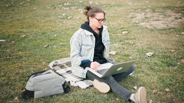 Young Woman Typing on Her Laptop While Sitting on the Lawn in the Park