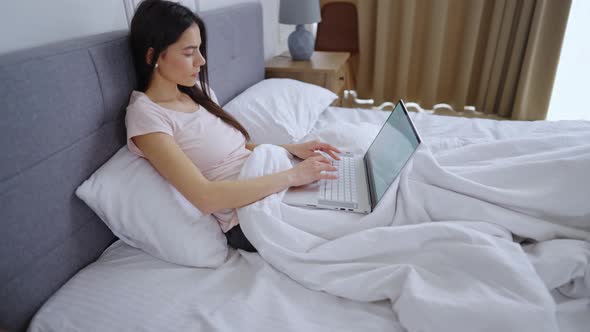 Young Girl Lies In Bed With Laptop