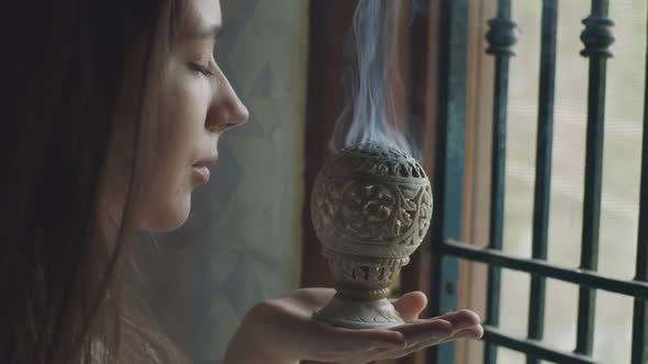 Side Portrait of Young Woman Smelling White Fume of Indian Censer Inside Temple. Pensive Girl