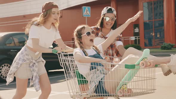 Three young beautiful models having fun in the grocery cart under the supermarket outdoors