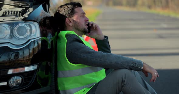 Young Man is Using the Phone in Asking for Help When His Car is Broken Man in a Green Safety Vest