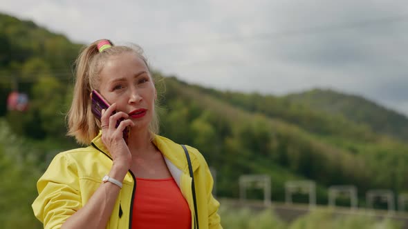 a Woman in Red and Yellow Clothes is Standing and Talking on the Phone Against the Background of