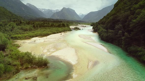 Aerial view of Soca river surrounded by many hills and vegetation in Slovenia.