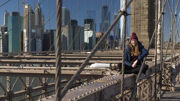 Young and Reckless Girl Sits on the Rim of Brooklyn Bridge New York