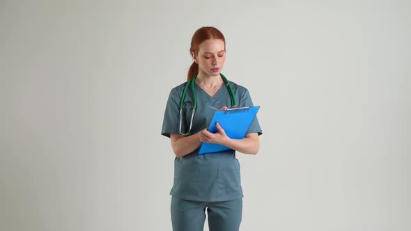 Portrait of Friendly Young Woman Nurse in Green Medical Uniform Talking While Writing Notes on