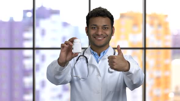 Cheerful Darkskinned Doctor Shows Bottle of Medicine and Thumb Up