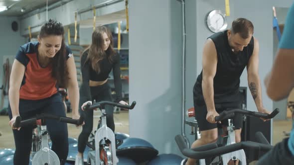 Unrecognizable Trainer Endorsing Men and Women Riding Exercise Bikes in Gym. Group of Sportive