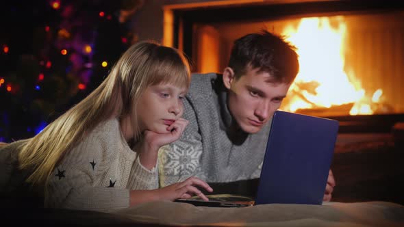 Brother and Sister Use a Laptop in the Living Room By the Fireplace
