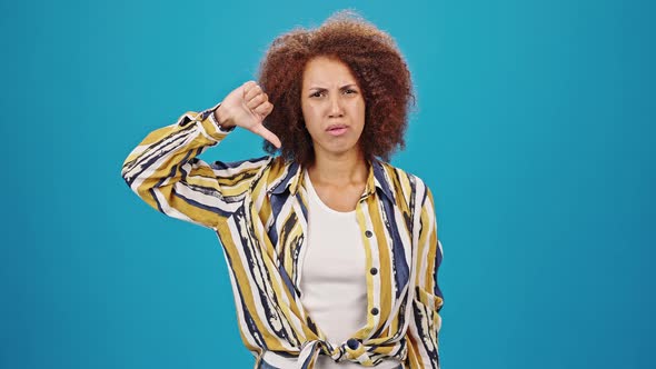 Dissatisfied Woman with Kinky Hair Makes Thumb Down Gesture