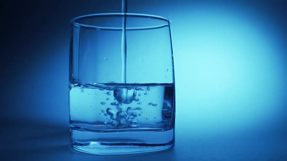 Studio Shoot of Water Pouring Into Transparent Glass on Blue Background