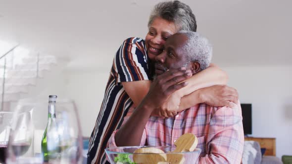 African american senior couple sitting by a table drinking wine eating dinner and hugging