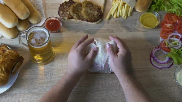 Fat Man's Hands Unpacking Fresh Burger and Carrying It to His Mouth, Greasy Food