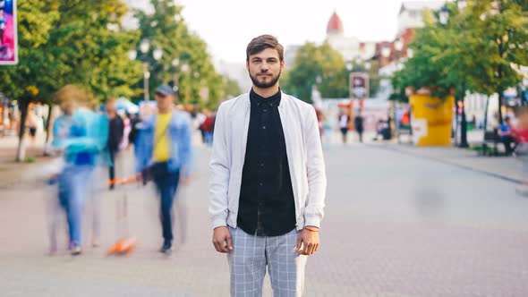 Zoom Out Time-lapse of Attractive Guy Standing in Crowded Street in City and Looking at Camera