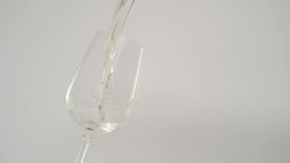 Slow Motion of Pouring White Wine in Tilted Glass White Background