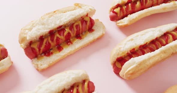 Video of hot dogs with mustard and ketchup on a pink surface