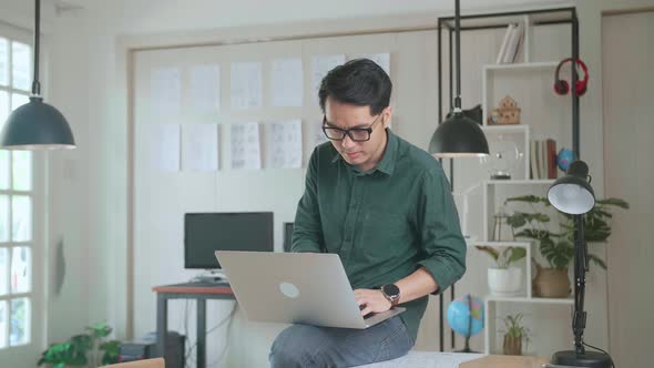 Creative Designer Sits On His Desk Holds Laptop On The Knees And Working On The Project