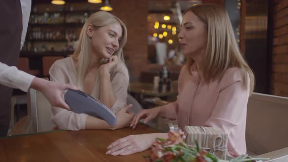 Happy Woman Chatting with her Adult Daughter and Paying in Cafe