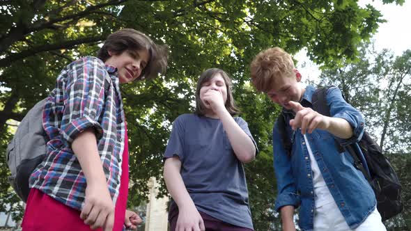 Bottom View of Three Schoolboys Pointing Down and Laughing at Camera. Aggressive Caucasian Boys