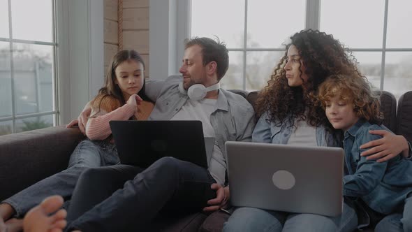 Young Family Sit Together on a Couch Hugging Talking and Looking at Laptops