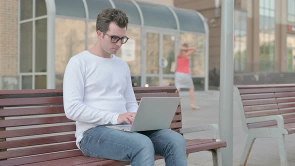 Busy Young Man Using Laptop Sitting Outdoor on Bench