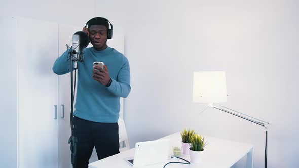 Man Wearing Headphones Singing a Song Into a Microphone in a Studio  Holding Phone