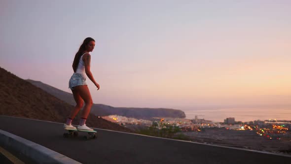 Beautiful Girl Rides a Skateboard on the Road Against the Sunset Sky