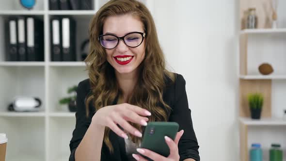 Young Businesswoman which Sitting at Her Workplace in Office Room and Using Phone