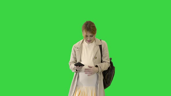 Pregnant Girl with Phone in Hand Walking on a Green Screen, Chroma Key.