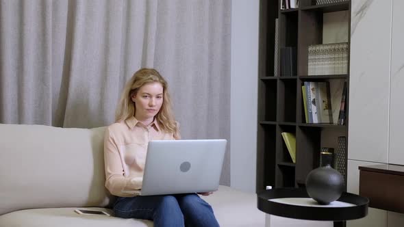 Girl works at home with a laptop on the couch in the room. Online work