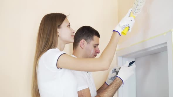 Young Happy Couple Decorating Room  Painting Wall with Paint Roller and Brush