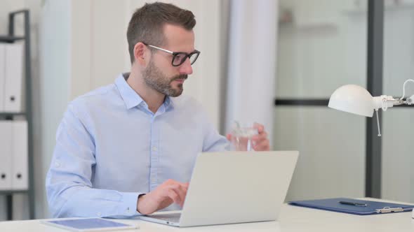 Middle Aged Man with Toothache Drinking Water While Using Laptop