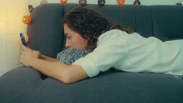 Young Woman is Using Smart Phone and Lying on Couch Leisurely in Living Room