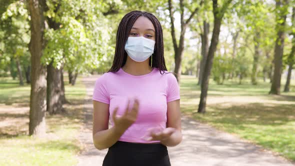 A Young Black Woman in a Face Mask Talks To the Camera in a Park on a Sunny Day